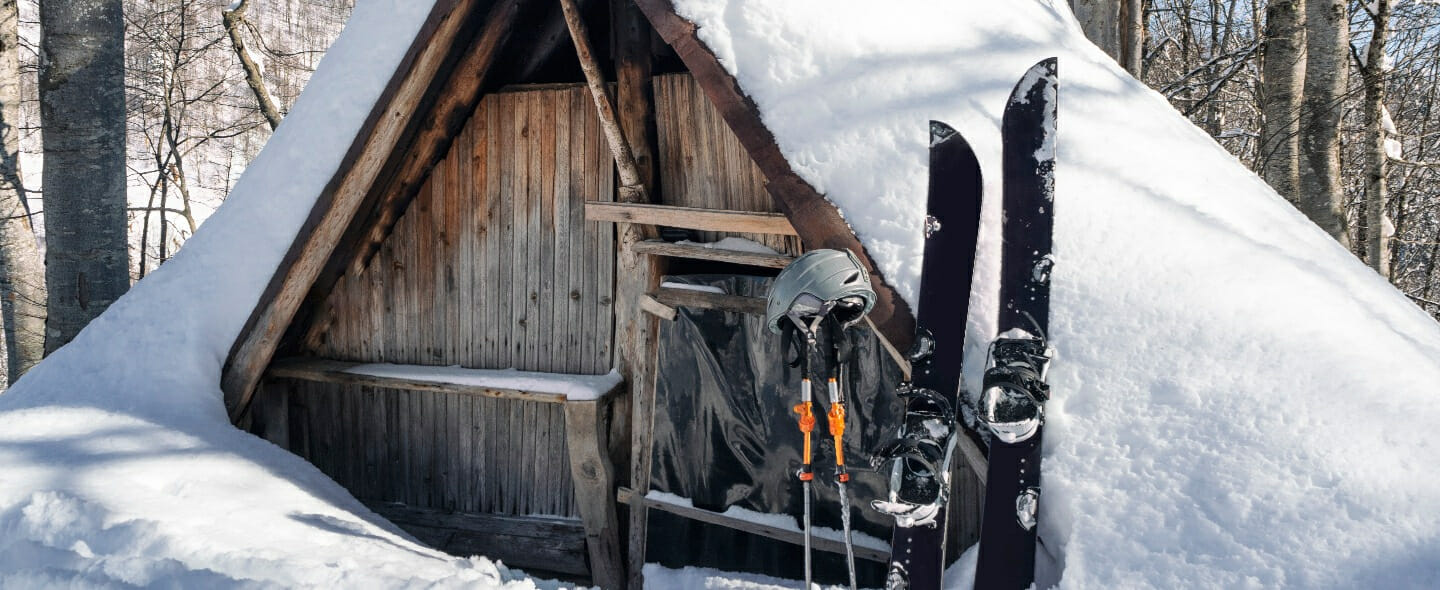 Splitboard Stöcke und Helm im Schnee vor einer Holzhütte